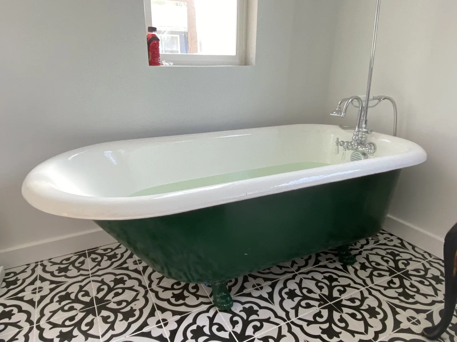 Restored forest green clawfoot tub with chrome shower riser on patterned cement tile