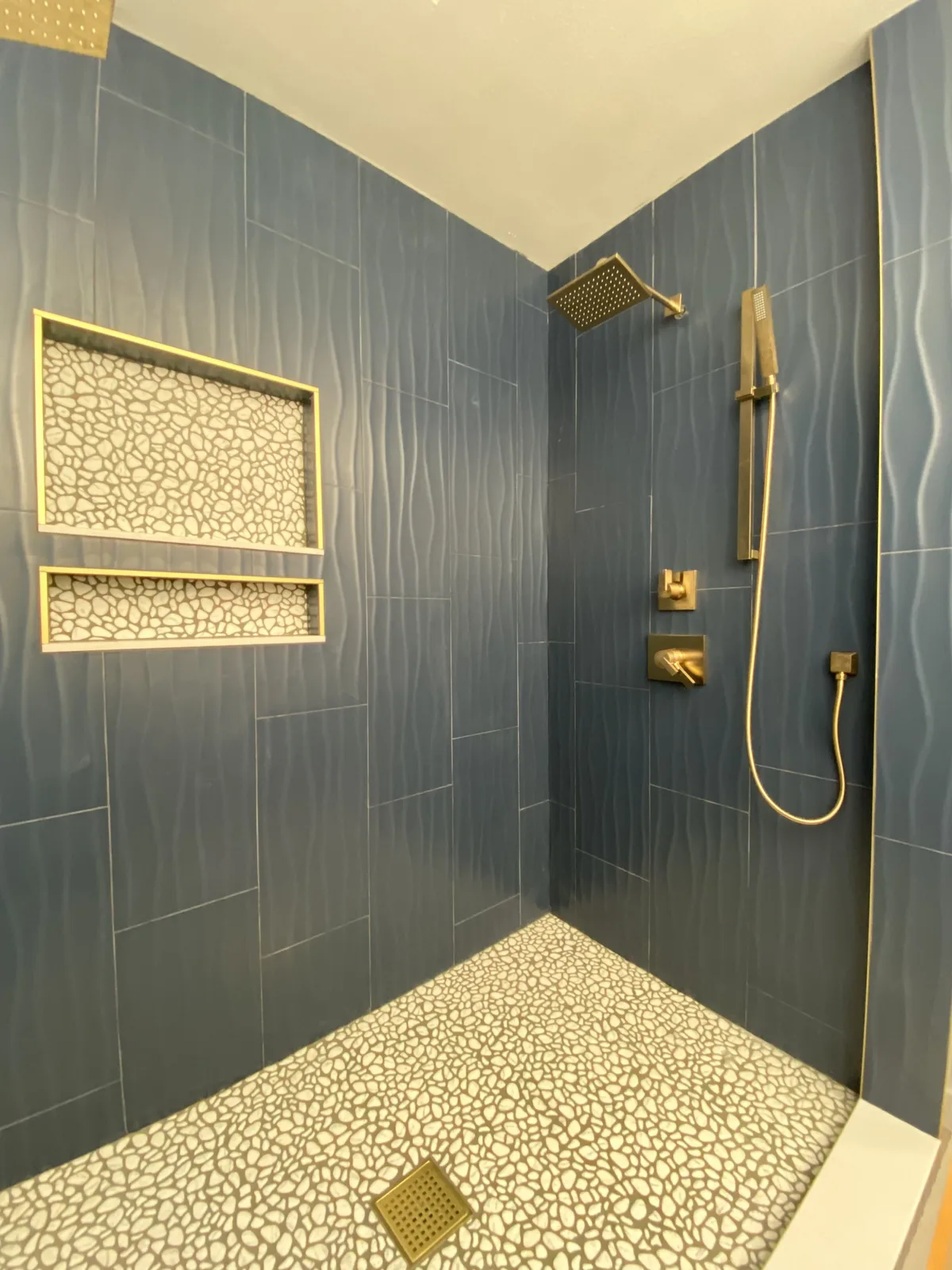 Brushed gold shower fixtures and tiled niches in a navy shower