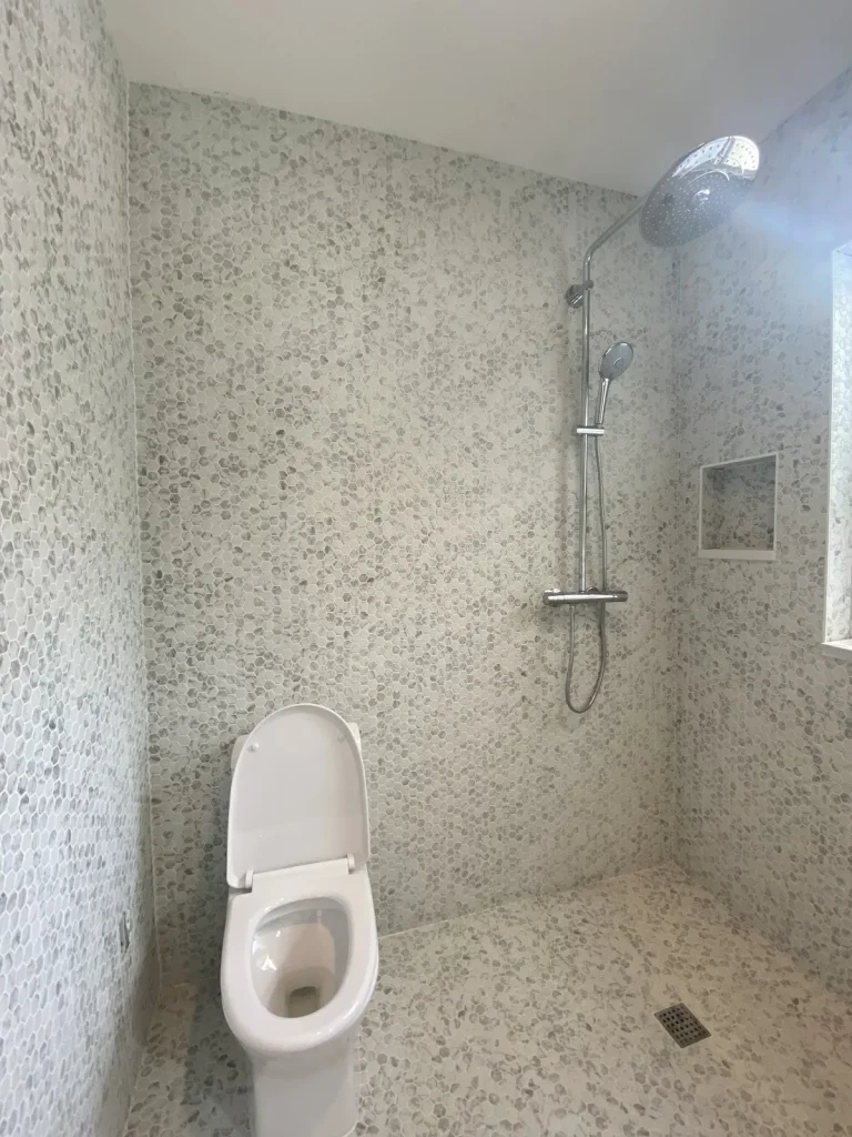 Curbless shower wrapped in marble hex mosaic with a chrome rain shower column