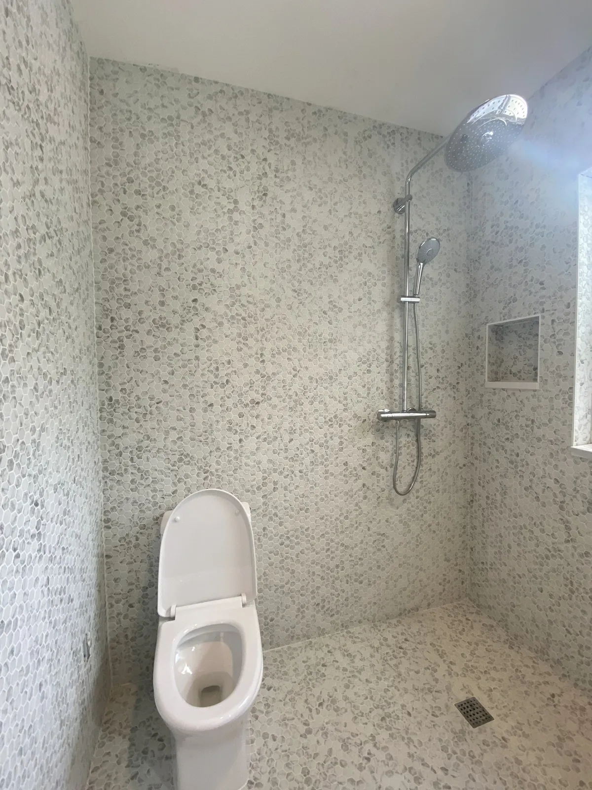 Curbless spa shower wrapped in marble hex mosaic with chrome rain shower column