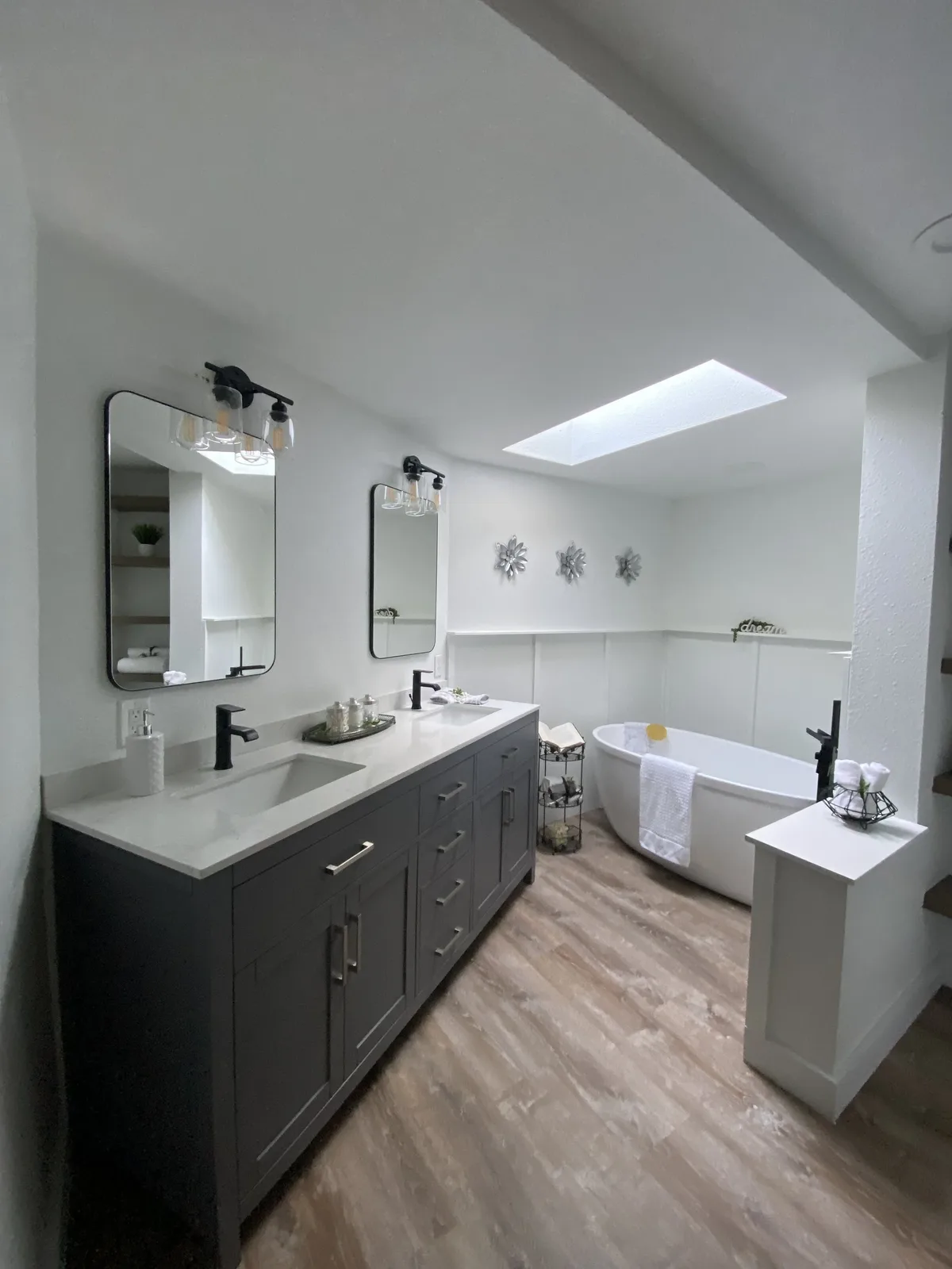 Master bathroom remodel with gray double vanity, freestanding soaker tub, and skylight