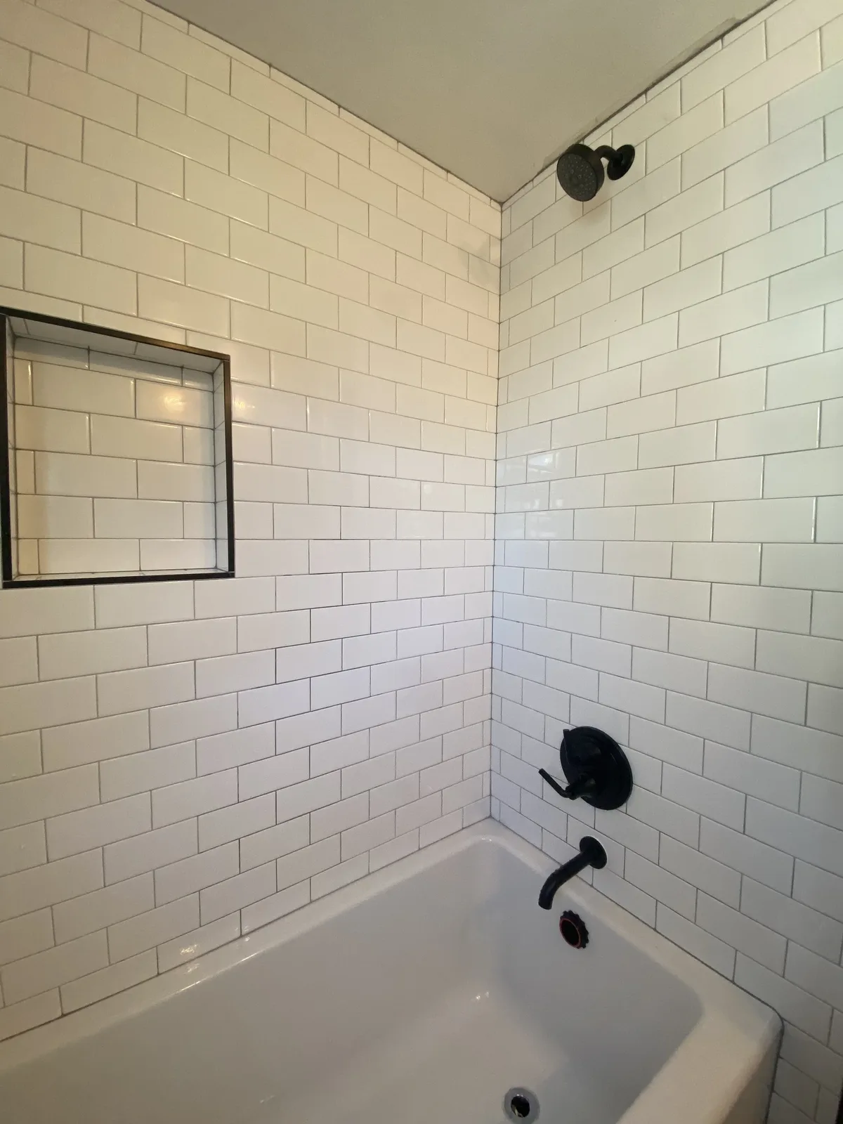 Subway tile shower with matte black valve, shower head, and tub spout